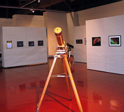 A Member Telescope stands before member astrophotos at the Las Cruces Fine Arts Museum